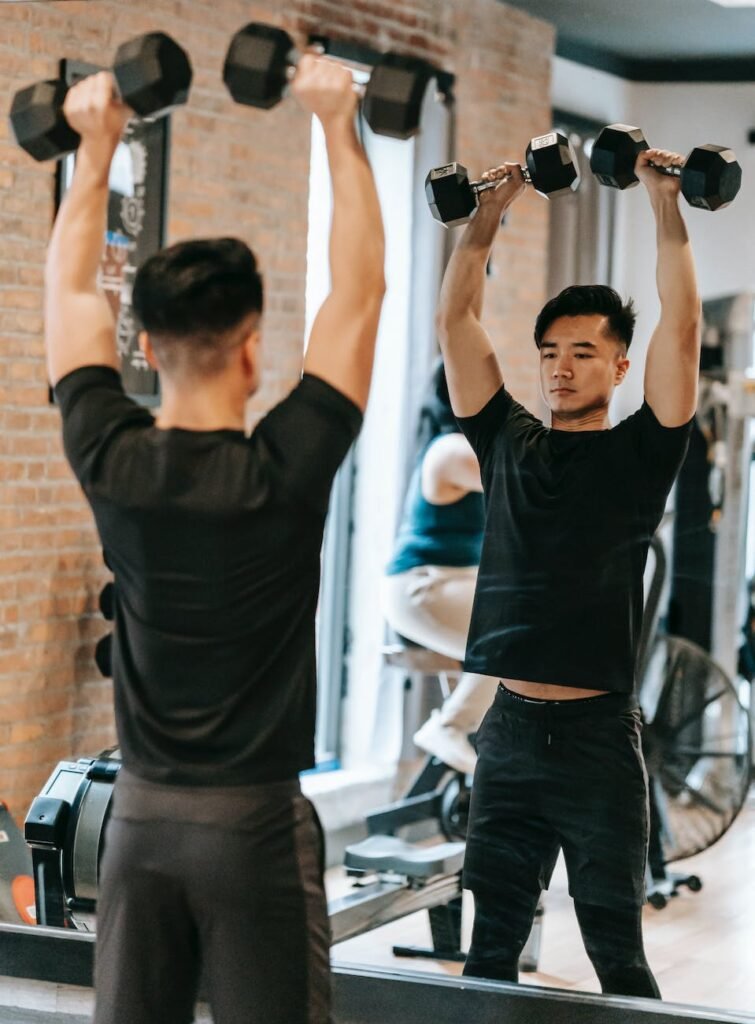 strong asian man raising dumbbells above head in gym